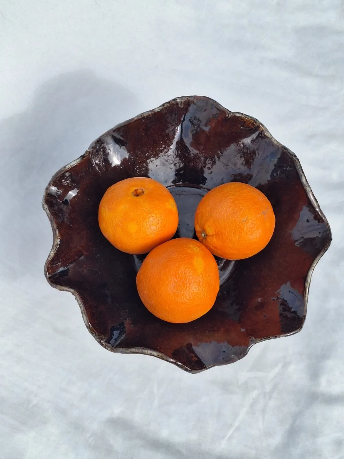 Ruffled dark-glazed bowl with oranges, seen from above