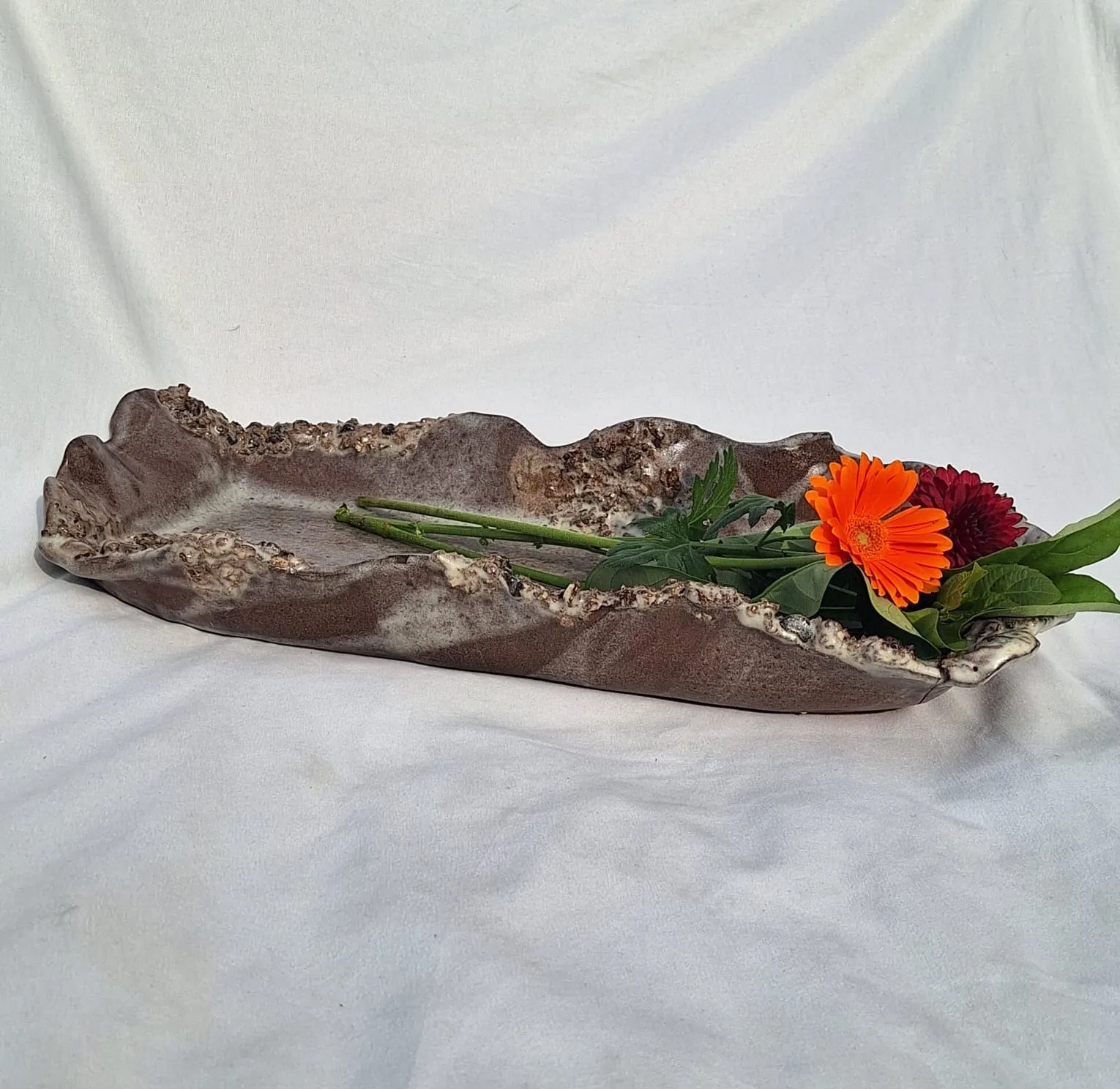 Hand-built ceramic platter with a rugged textured rim, holding fresh flowers