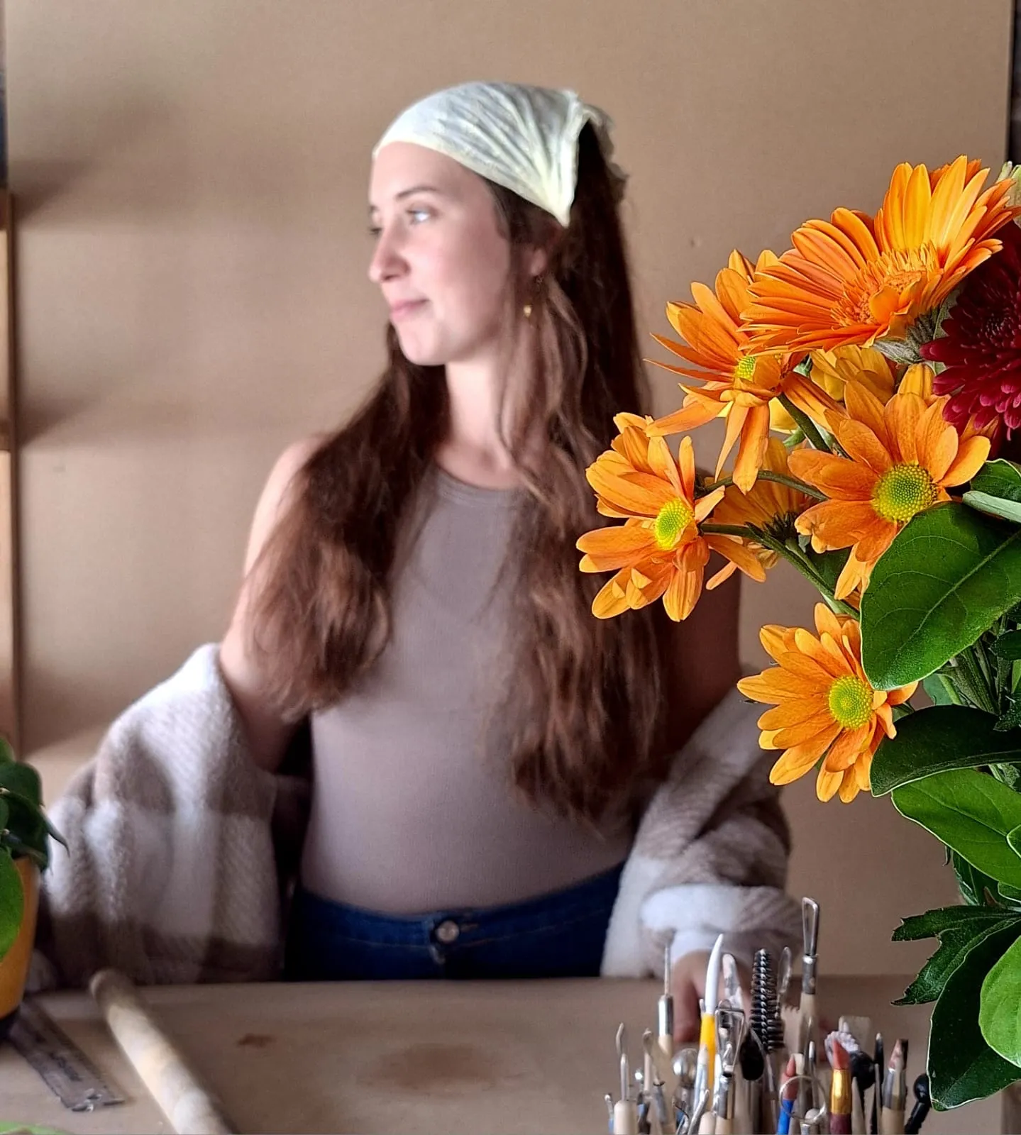 Marí, the potter behind Clay by Mari, at her workbench with clay tools and fresh flowers