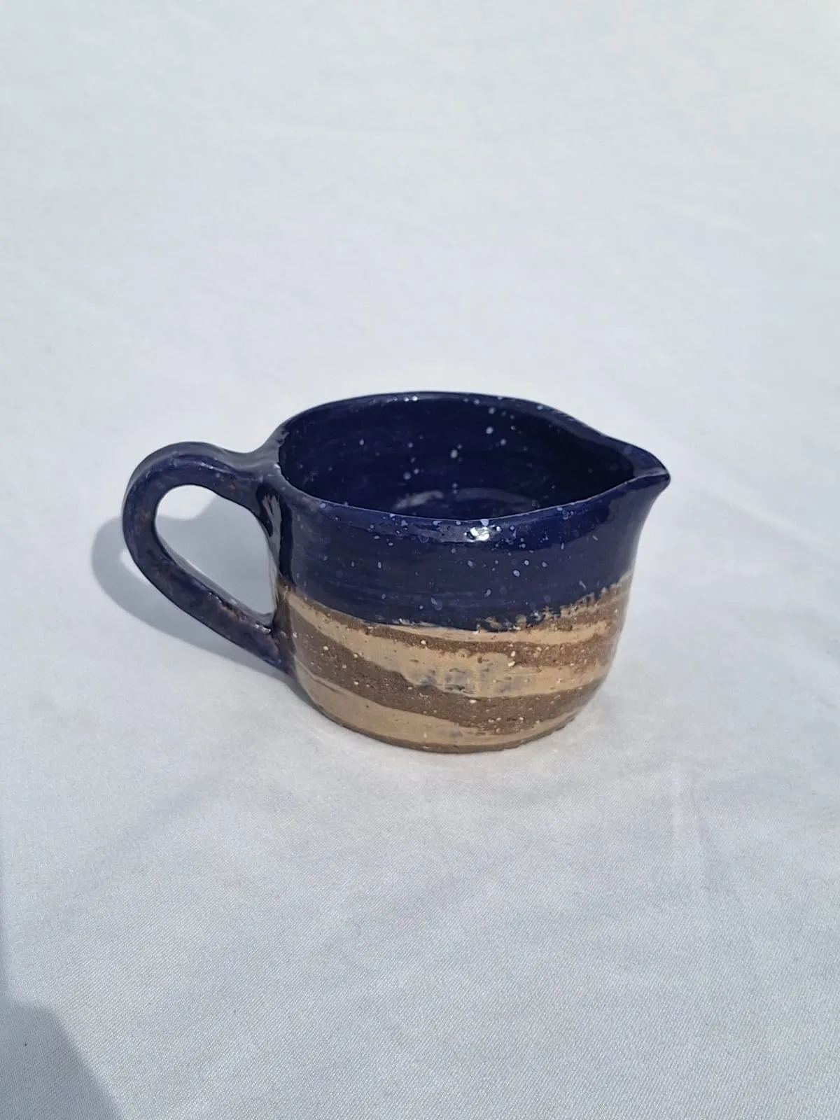 The galaxy milk jug — A small jug in deep speckled cobalt over raw marbled clay.